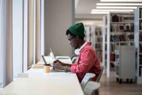 オンラインライブラリデータベース サイドビューを使用してノートパソコンでデスクに座っているフォーカス黒人男性 アフリカ系アメリカ人の男性学生は 大学試験の準備をしながらコースワークを書く 教育概念におけるインターネット — ストック写真