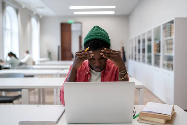 コンピュータの仕事の後緊張片頭痛を持つ疲れた黒人のフリーランサー男性 疲れアフリカ系アメリカ人学生男とともにラップトップタッチヘッド感じ不健康なから難しい研究で大学図書館 — ストック写真