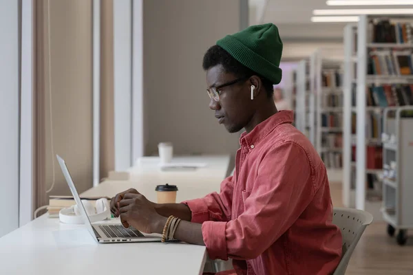 集中アフリカ系アメリカ人のスタイリッシュな男性は 公共図書館のパノラマウィンドウの近くのラップトップにメッセージを書き込みます オンラインで通信する黒の焦点の男は遠くで働くか コンピュータ上で勉強電子メールを送信 — ストック写真