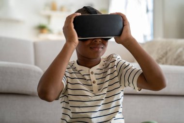 Sanal gerçeklik gözlüğü takan meraklı Afrikalı Amerikalı çocuk evde sanal dünya simülasyonu çalışıyor. Ciddi küçük okul çocuğu VR gözlükleriyle eğitim konusunda deneyim kazandı.