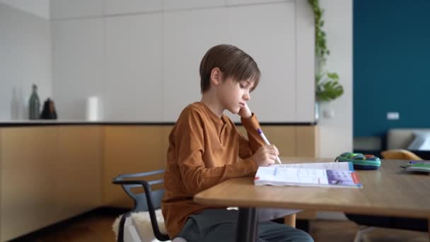家庭で勉強している不幸な少年は 宿題をしている間に台所のテーブルに座って退屈し 悲しい子供は外国語を学ぶことに苦労し 宿題時間中にフラストレーションを経験します — ストック動画