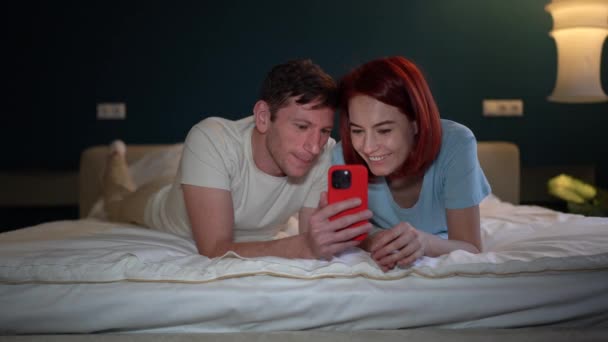 Zorgeloos Ontspannen Echtpaar Liggend Bed Kijkend Naar Grappige Video Sociale — Stockvideo
