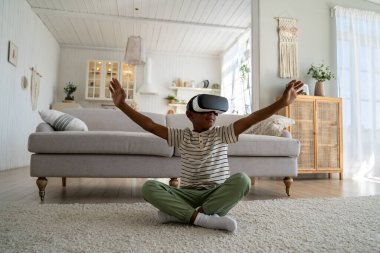 Dijital çocuk. Küçük Afrikalı Amerikalı çocuk VR simülasyon oyunu oynuyor, meraklı okul çocuğu sanal ve artırılmış gerçeklikte gezegenleri keşfediyor, yerde oturuyor ve palmiyelerle havaya dokunuyor.