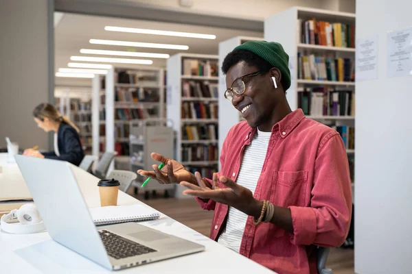 愉快地满意的非裔美国人学生或自由职业者的手势与双手对话使用笔记本电脑举行视频会议 用电视教育的方式微笑坐在图书馆里的黑人 — 图库照片