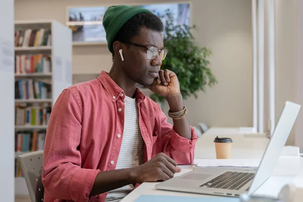 アフリカ系アメリカ人の男性家庭教師に焦点を当て 図書館のオンラインクラスのためのノートパソコンの準備を見て 教師や学習のためのコンピュータを使用して集中黒人男性 距離教育の概念 — ストック写真