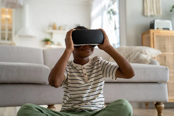 stock image Curious African American kid boy wearing virtual reality 3D glasses online study simulation virtual world at home. Serious small schoolboy get experience in education knowledge with help VR goggles