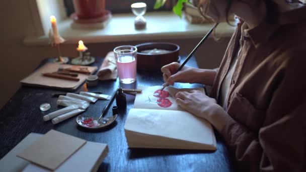 创意业余爱好 接近女性艺术家坐在桌旁 在家中或工作室的素描本上燃着蜡烛 使用油画 年轻的女天才画家创作新的艺术作品 — 图库视频影像