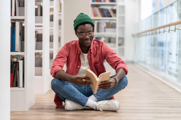 快乐的非裔美国人千禧年 戴着眼镜 手拿书本坐在地板上 参观图书馆 学生们选择文学 在书店笑一个黑人阅读业余爱好 自我教育 — 图库照片