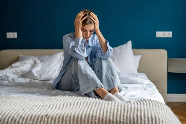 Upset depressed woman sitting on bed hold head in hands lost in thoughts thinking of problem solution. Worried devastated unhappy young female suffering from personal trouble need psychological help