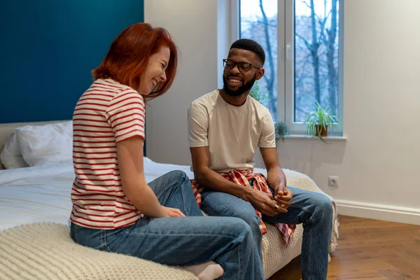 関係におけるコミュニケーション 若い異人種間のカップル男と女笑いながらベッドに座って話をしながら 家で夜の間に良い会話をし パートナーとの結合 — ストック写真