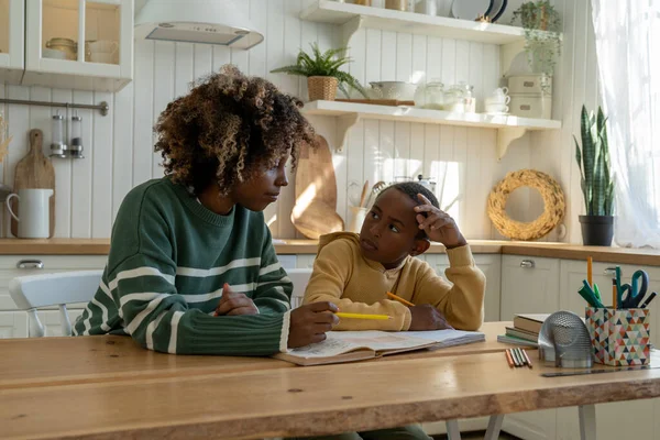 在家学习 非洲裔美国母亲坐在孩子身边 帮助他做家庭作业 不安的学童在家里学习时让妈妈帮忙做数学 父母对学习的支持 — 图库照片