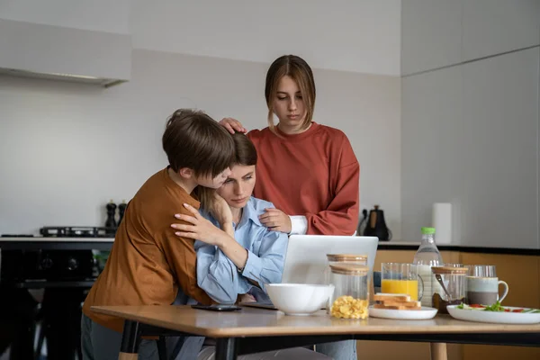 Loving children supporting hugging single mother struggling to find job. Upset unhappy family mom and two kids embracing looking at laptop screen. Son and daughter support upset mum lost job