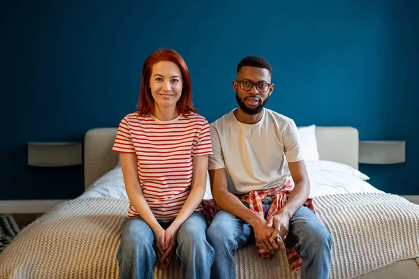 幸せなだけで結婚した異人種間のさまざまなカップルの家でベッドの上に一緒に座っている間 カメラで笑顔の肖像画は 新しい近代的なスタジオアパートメントに移動しました 調和のとれた家族関係の概念 — ストック写真