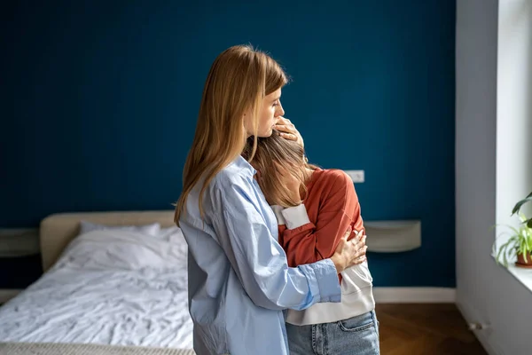 Mother hugging comforting upset crying teenage daughter at home, single mom showing love support to sad worried child, embracing and supporting teen girl, helping to cope with first love heartbreak