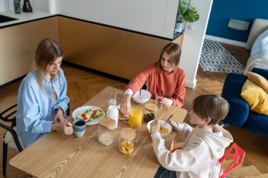 Ailenin sağlıklı kahvaltısı. Kardeşler anneleriyle birlikte sabahları mutfak masasında otururlar. Amerikan yemeği. Sütlü mısır gevreği, portakal suyu, sandviç. Ergen kızı ve oğluyla ilgilenen anne, okuldan önce yemek yer.