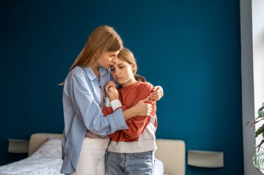Affectionate empathic young mom tender embracing calming quieting down lost, upset or grieving teen daughter helping and supporting. Mother comforting and consoling girl. Teenage problems concept. clipart