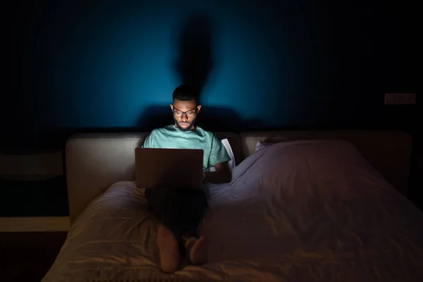 Schwarzer Arbeitet Laptop Liegt Nachts Bett Und Blickt Aufmerksam Auf — Stockfoto
