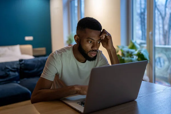 アフリカ系アメリカ人の男に焦点を当て 自宅でラップトップを使用してフリーランス 自宅のオフィスで一晩中プロジェクトに取り組んで過労した黒人男性 学生の男は コンピュータ画面を見てリモート研究疲れて感じている — ストック写真