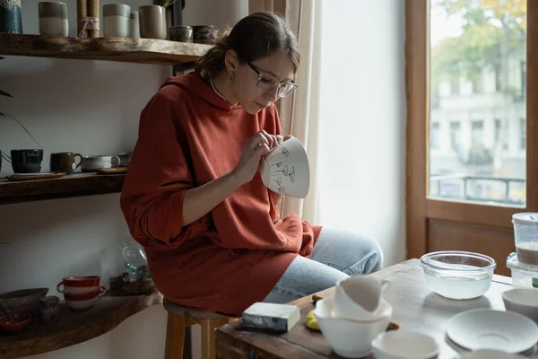 創造的な女性アーティストは 手作りの粘土板にパターンを適用する独自のワークショップ絵画でテーブルに座っている 難しい仕事の週の後にストレスを取り除くために陶器の製造に従事する集中した女の子 — ストック写真