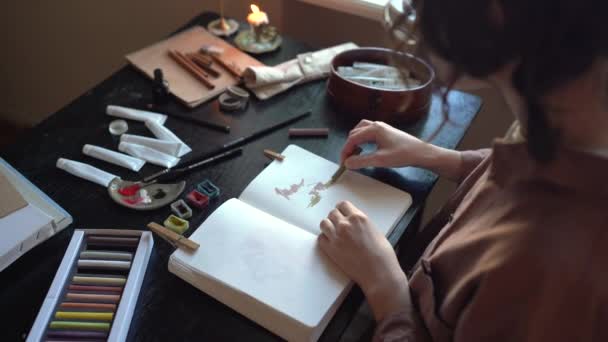 女性の絵は アートスタジオのテーブルに座ってパステルチョークを使って絵を描く スケッチブックの女の子の絵画は 塗料のスキルを練習 燃えるろうそくとロマンチックな雰囲気 大学美術学生 — ストック動画