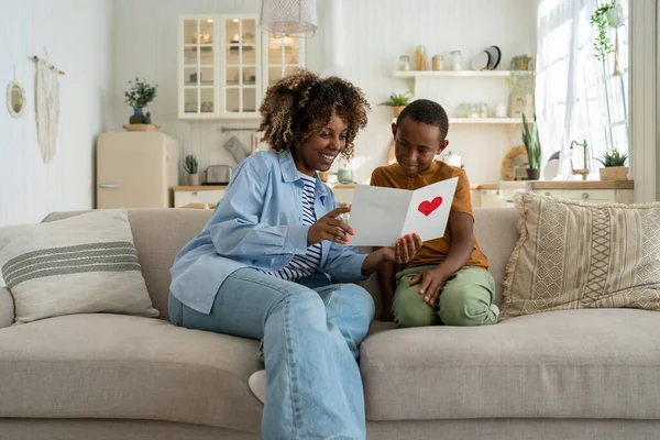 アフリカ系アメリカ人の息子の世話休日のイベント 母の日や誕生日のためのお母さんのグリーティングカードは お母さんの読書はがきの近くに座っている 幸せな若いですシングルママ読書バレンタインとともに子 — ストック写真