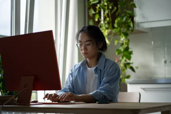 奨学金申請のためのエッセイを入力する集中アジアの女性学生は無料教育を取得したいと考えています 注目すべき焦点を当てた中国の女の子フリーランスは 自宅のオフィスでコンピュータと作業机の上に座って — ストック写真