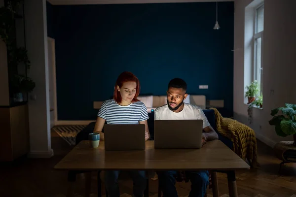 夜遅くにコンピュータを使用してオンライン家族経営の家庭 アフリカの男性と原因アジアの女性の所有者で一緒にオンラインで働くフリーランスの包括的な多様なカップルは 残業フリーランスの仕事をやって — ストック写真