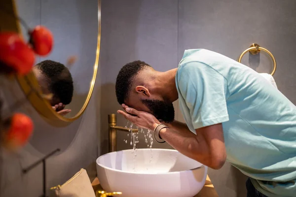 男性のためのスキンケアルーチン アフリカ系アメリカ人の何千人もの男が朝に皮膚を洗浄し浴室の上に立って水で顔を洗って目を覚ますしようとしています — ストック写真