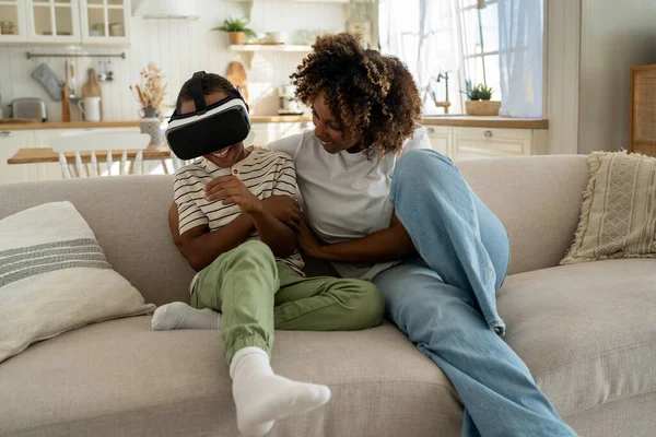 幸せなアフリカ系アメリカ人の母親と息子は ビデオゲームのために仮想メガネを使用しています 少年は自宅でソファに座ってVrヘルメットで仮想世界を見て 仮想現実 サイバー空間 エンターテイメントの概念 — ストック写真