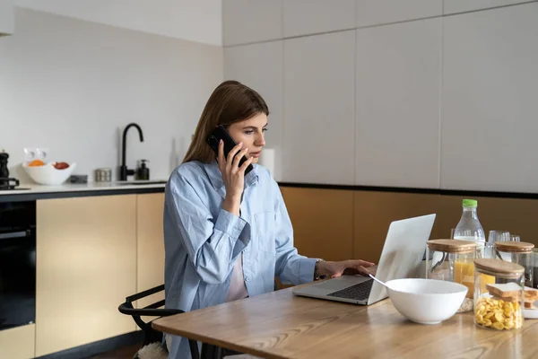 Young Woman Sitting Kitchen Table Using Laptop Computer Talking Phone — Stock Photo, Image