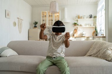 Odaklanmış Afrikalı Amerikalı çocuk sanal gerçeklik kulaklığıyla araba sürüyor. Siber uzayda hareket eden meraklı gençler evdeki kanepede oturuyor. Boş zaman, eğlence konsepti.