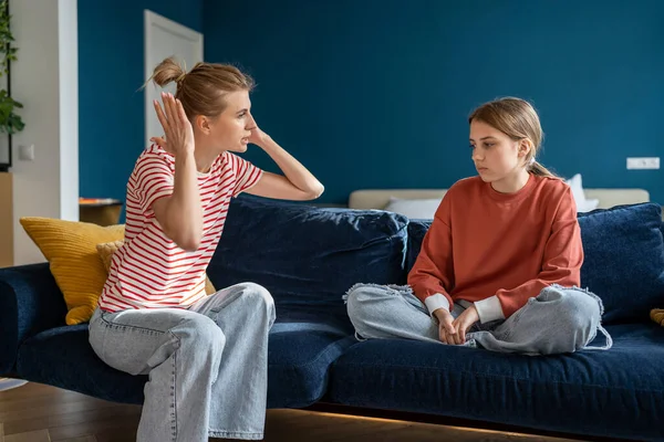 10代の娘に自宅のソファに座って叫んで身動きのない母親ジェスチャー 悲しい10代の女の子はお母さんを見る ティーンエイジャーとの関係の問題 相互誤解と世代間のギャップの概念 — ストック写真