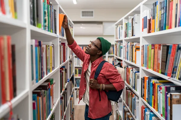 大学図書館で本を選ぶアフリカ系アメリカ人のオタク学生 大学を勉強バックパック付きの賢明な男ヒップスター 新しい職業の提供 学習コンセプト — ストック写真