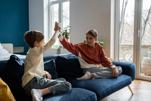 幸せな子供たち兄弟は 家で一緒に遊んでいる間に高5を与え 姉は弟と一緒に時間を過ごし リビングルームでソファに座って楽しい時間を過ごしています — ストック写真