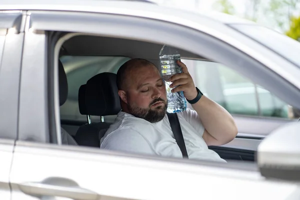 暑い夏の天候で壊れたエアコン付きの車を運転する疲れた太りすぎの男 男性は ムッとする苦しみを冷却するために直面する水のボトルを押す 疲れきった過熱した男 — ストック写真