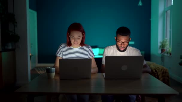 在同一个项目中 不同类型的夫妻与笔记本电脑一起工作 彼此交流思想 晚上在家里坐在桌旁 忙碌的黑人男子向欧洲女人展示计算机上的信息 — 图库视频影像