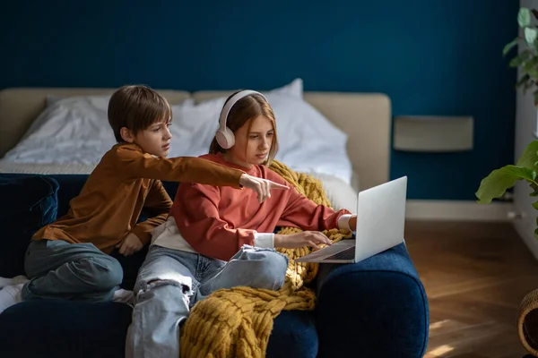 戴耳机的少女姐姐和坐在家里沙发上一起看电影的兄妹 男孩指着屏幕上的东西 数码娱乐 娱乐概念 — 图库照片