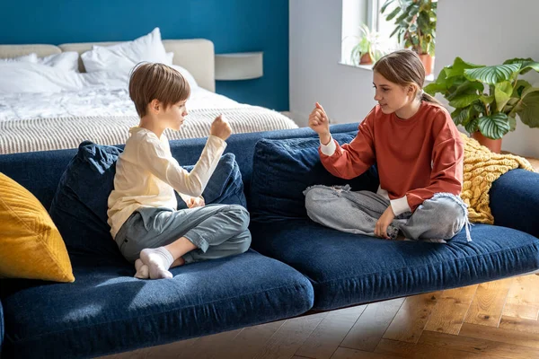 友爱的弟妹弟妹玩石纸剪子游戏 坐在家里卧室的沙发上 孩子们一起玩手指游戏 有趣的娱乐活动 家庭友谊 — 图库照片