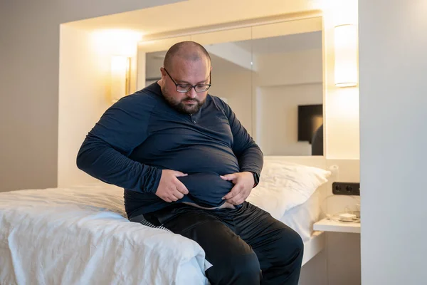 Man Lijdt Aan Extra Gewicht Raken Buik Zittend Bed Slaapkamer — Stockfoto
