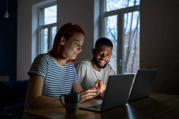 現代の笑顔多人種家族カップル妻と夫はフリーランスを楽しみます 一緒にノートパソコンで作業テーブルに座って 幸せなアフリカ人男性と白人女性は自宅から成功したオンラインビジネスを実行します — ストック写真