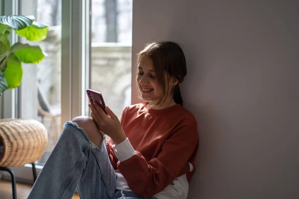 Neşeli Mutlu Genç Kız Akıllı Telefonuyla Yerde Oturuyor Mesaj Mesajları — Stok fotoğraf