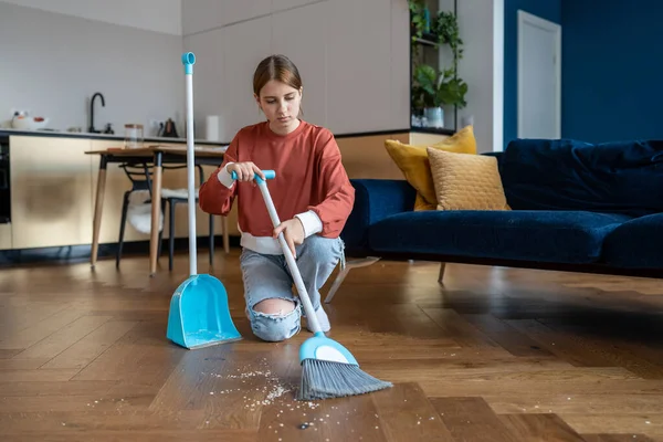 十代の女の子は掃除の家の親を助けながら リビングルームでほうきで床を掃除 簡単な家事をしています 10代の子供は疲れ果て家をきれいにする — ストック写真