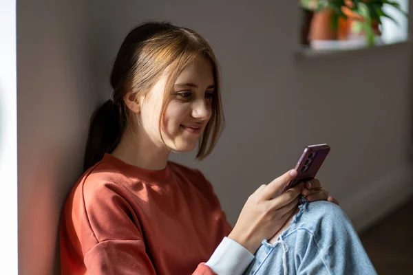 즐거운 미소를 소녀는 스크린 미디어에서 스마트폰으로 메시지를 받으며 바닥에 관심있는 — 스톡 사진