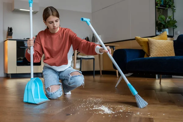 独立した10代 子供の頃からクリーニングハウスの習慣 焦点を当てた10代の女の子は ブラシとダストパンとほうきで散乱破片から床を掃引します 青年は家事をし 国内の掃除をする — ストック写真