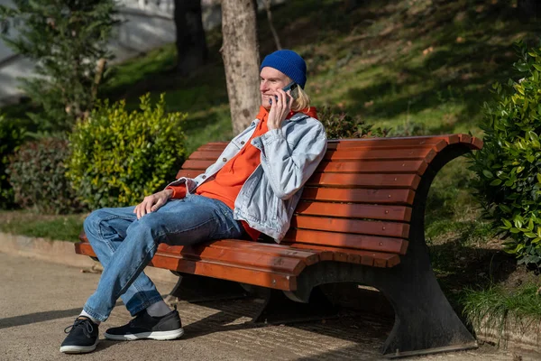 Щасливий Хіпстер Розмовляє Мобільному Телефоні Сидячи Лавці Парку Усміхаючись Тисячоліття — стокове фото