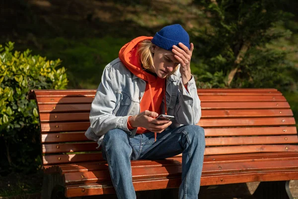 Haberler Kötü Milenyum Çocuğu Parkta Bankta Oturmuş Elinde Akıllı Telefonuyla — Stok fotoğraf