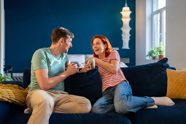 カップコーヒー ボンディングでソファでリラックスしながら笑いを冗談を愛する幸せなカップルは 自宅で一緒に瞬間を楽しんでいます 関係における感情的なつながり — ストック写真
