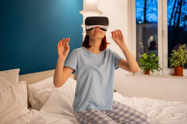 ベッドの上の仮想現実のメガネを使用して女性 女の子は特別なデバイス ヘルメットシミュレータを介してビデオゲームをプレイします Vrゲームのための特別なメガネを身に着けている幸せな女性は現実世界を探索しない — ストック写真