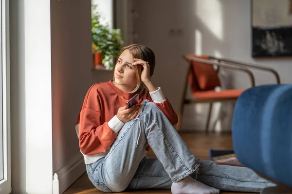 Pensive Girl Teenager Sits Floor Looks Window Home Holding Smartphone — Stock Photo, Image