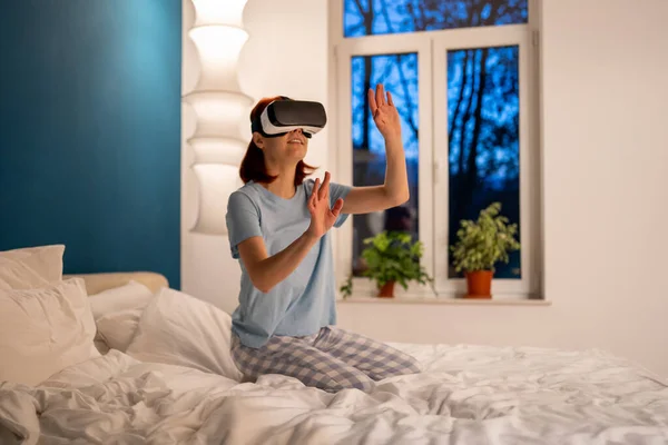 兴奋的笑着的女人戴著虚拟眼镜看电影玩游戏 高加索女性穿着Vr头盔坐在床上看着虚拟世界 网络空间 娱乐概念 — 图库照片
